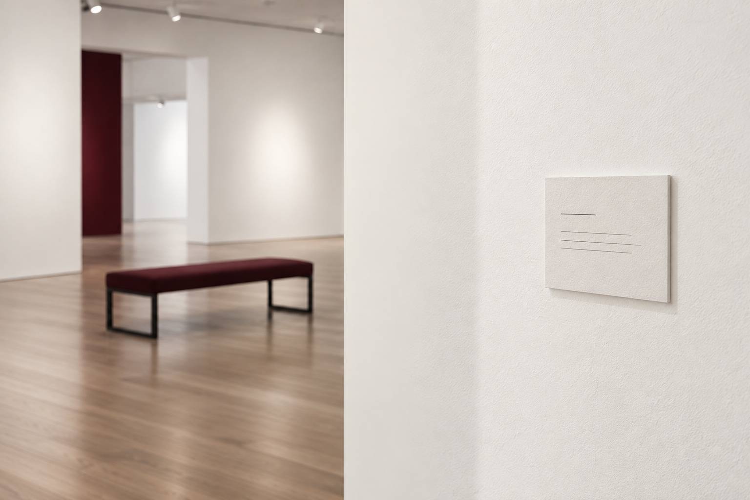 Détail d'une cimaise blanche avec cartel d'exposition illisible et banc de musée